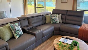 A modern living room with a sectional sofa, a small side table, and a round coffee table with plants. - Wangi Waterfront Escape, Walk to Cafes, Parks & Lake Reserve (Wangi Wangi)