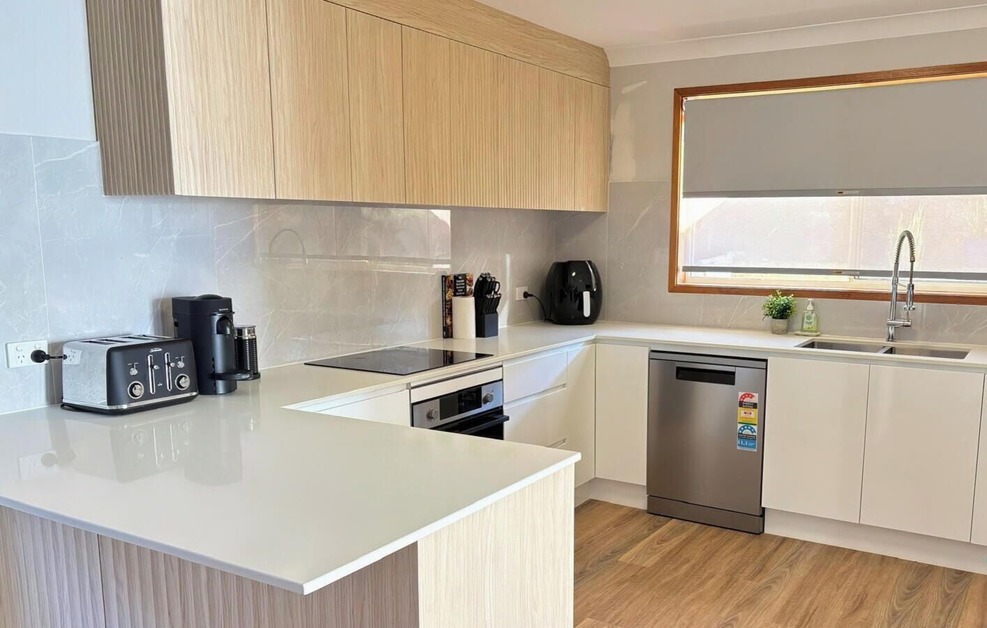 Een moderne keuken met een aanrecht, een broodrooster, een koffiezetapparaat, een vaatwasser en een raam boven de gootsteen.