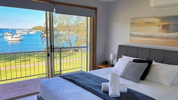 A hotel room with a bed, a nightstand, a lamp, and a painting. - Wangi Waterfront Escape, Walk to Cafes, Parks & Lake Reserve (Wangi Wangi)