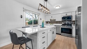 A modern kitchen with white cabinetry, a central island with bar stools, a built-in oven, and a stainless steel refrigerator. - In-Ground Pool AND Hot Tub! Fenced Yard, Pet Friendly Home. Near Town! (Crystal Lake)