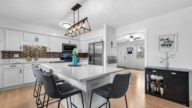 A modern kitchen with white cabinets, a large island with bar stools, a built-in wine rack, and a pendant light. - In-Ground Pool AND Hot Tub! Fenced Yard, Pet Friendly Home. Near Town! (Crystal Lake)