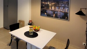 Ein Essbereich mit einem weißen Tisch, schwarzen Stühlen und Pendelleuchten. An der Wand hängt ein Stadtbild.