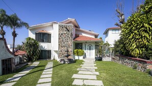 Une maison à deux étages avec une façade en pierre, un toit en tuiles et une pelouse bien entretenue, ponctuée de pierres plates qui mènent à la porte d’entrée.