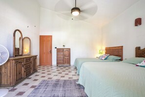 A bedroom with two beds, a wooden dresser, a mirror, a ceiling fan, and a door.