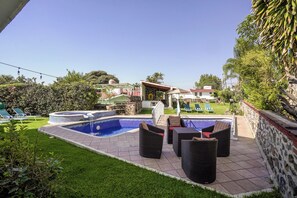 A backyard with a swimming pool, lounge chairs, and a stone wall.