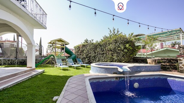 Un espace piscine équipé d’un toboggan, de chaises longues et d’une petite structure de jeux.