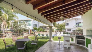 Une terrasse extérieure avec une table et des chaises, un barbecue, et une piscine en arrière-plan.