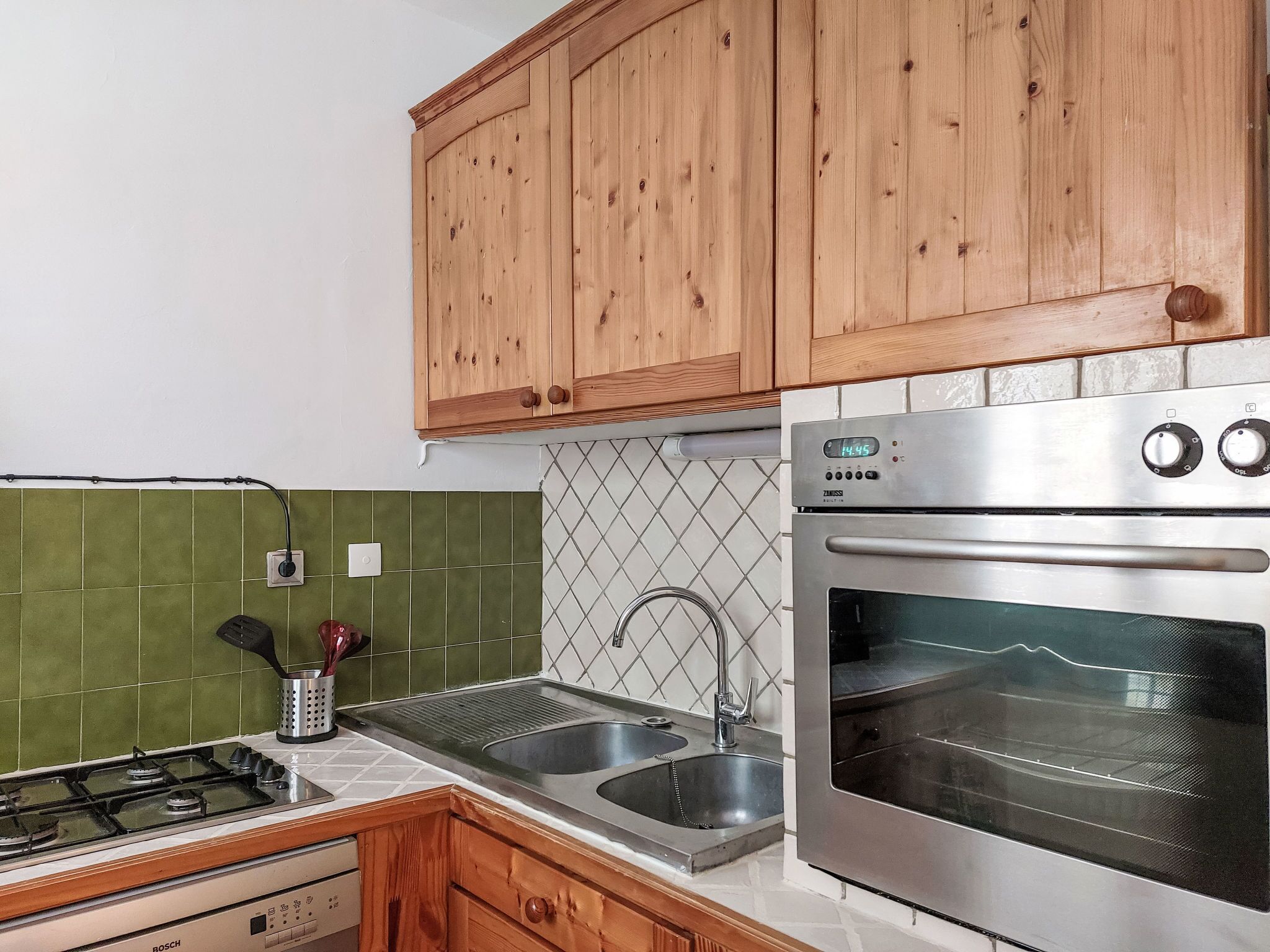 Een keuken met houten kastjes, een Bosch gasfornuis, een spoelbak en een roestvrijstalen oven.
