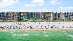 Un hotel frente a la playa con varios edificios altos, una playa de arena con muchos sombrillas y una vista despejada del océano.