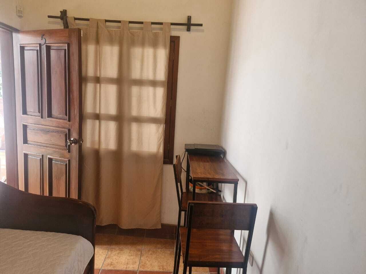 Una stanza con un letto, una scrivania con una sedia, una porta in legno e una tenda.
