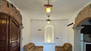 A spacious room with two sofas facing a large arched window, a wooden door, and a stone pillar. - Cozy Colonial Style Azotea Apartments (Jocotenango)