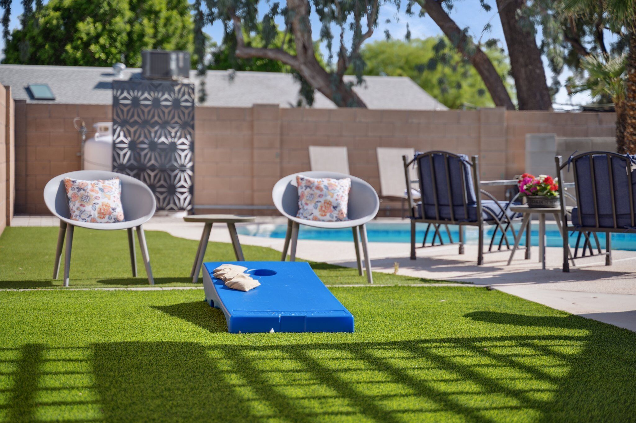 A poolside area with a blue lounge chair, two white lounge chairs with floral cushions, and a table with chairs.