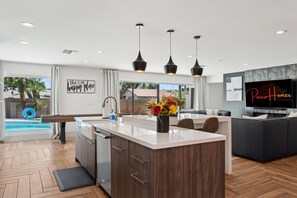 Una cucina moderna con isola centrale, illuminazione a sospensione e un grande televisore.