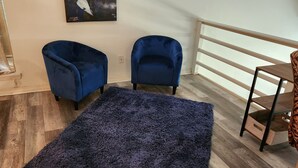 A room with two blue armchairs, a dark blue rug, a wooden floor, a white railing, and a piece of wall art. - Charming 2-bedroom home with fenced yard sleeps 6 in Baton Rouge near Tigerland (Baton Rouge)