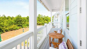 A covered outdoor area with a table and chairs, a white railing, and a view of greenery.