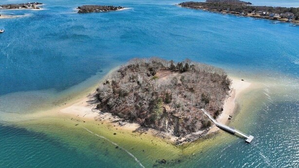 An aerial view of a small island with a dock, surrounded by clear blue waters and distant landforms. - Beach, Breeze & Bunk Beds. FamilyFun Steps to the Shore. Dog-Friendly, GameWall. (Wareham)