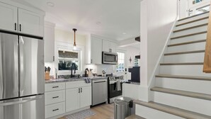 A modern kitchen with stainless steel appliances, white cabinetry, and a wooden staircase. - Beach, Breeze & Bunk Beds. FamilyFun Steps to the Shore. Dog-Friendly, GameWall. (Wareham)