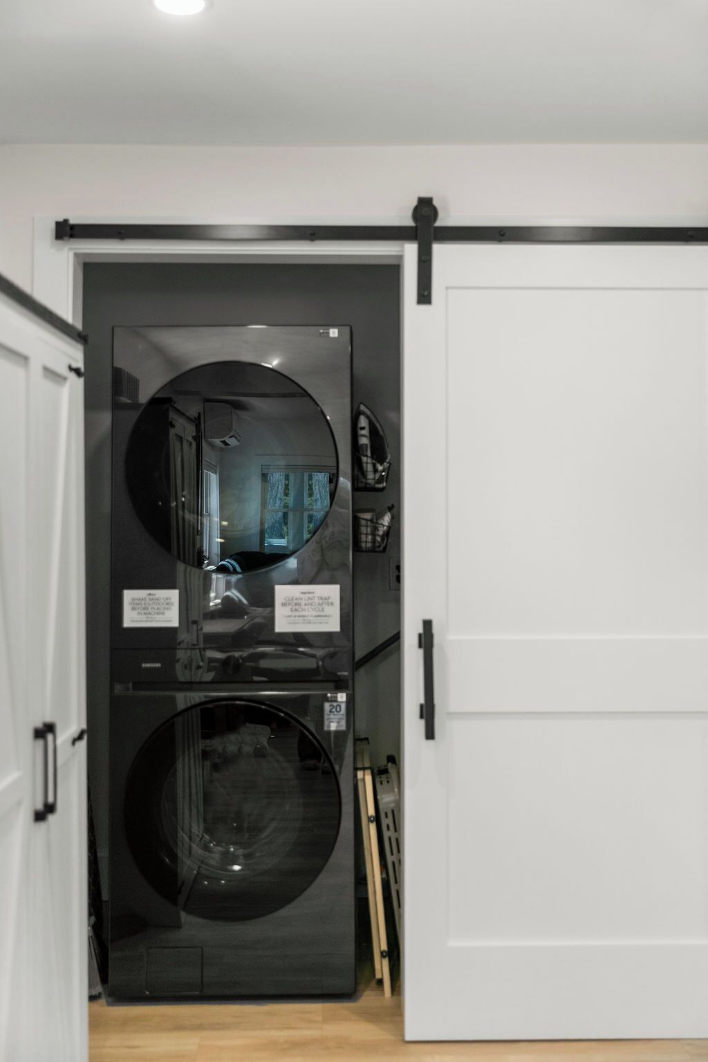 Une petite buanderie équipée d’un grand lave-linge et d’un grand sèche-linge, avec une porte blanche et une porte coulissante noire.