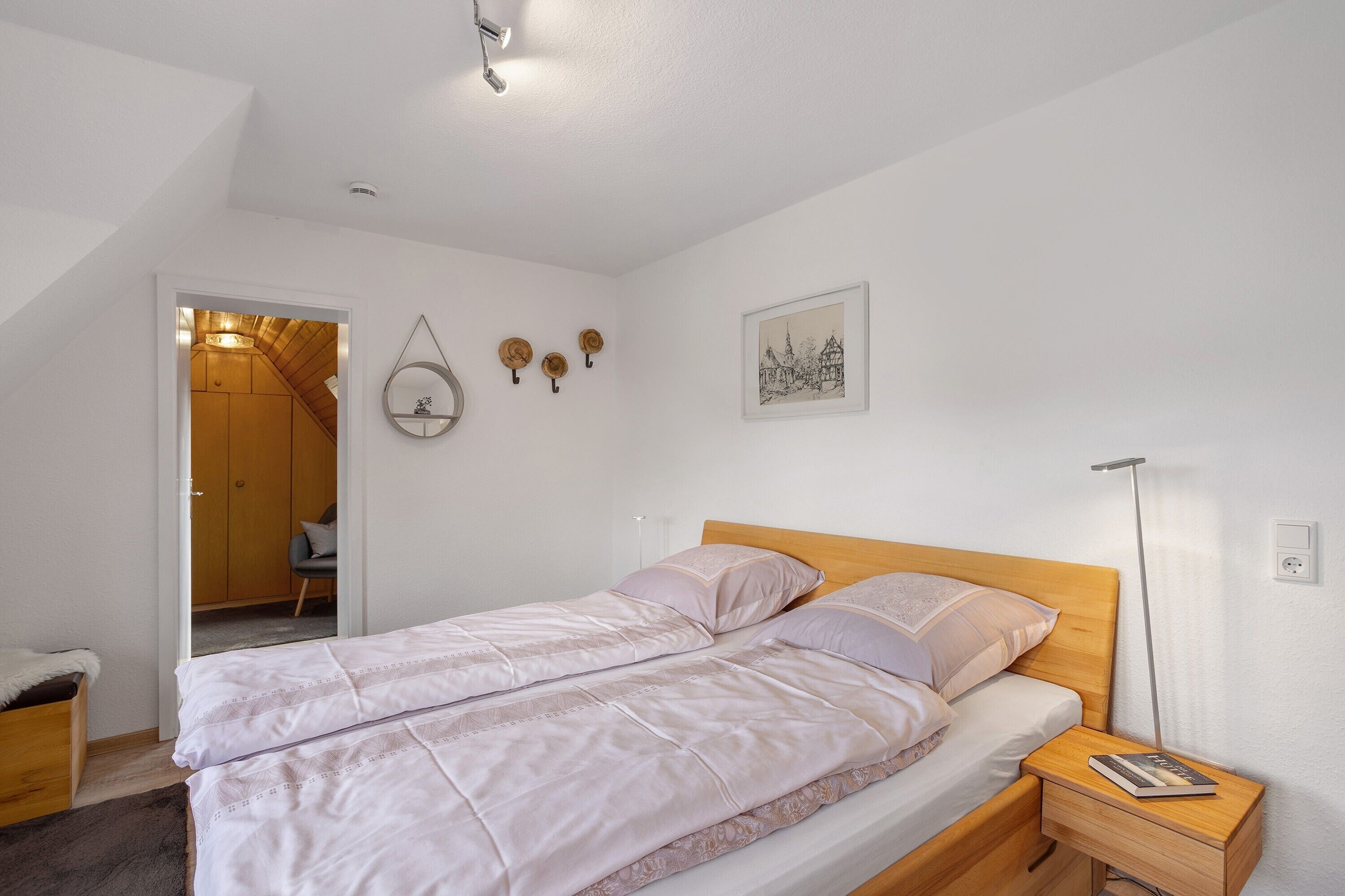 Ein Schlafzimmer mit Bett, Nachttischen, einer Stehlampe, einer Tür zu einem anderen Raum und Wanddekoration.