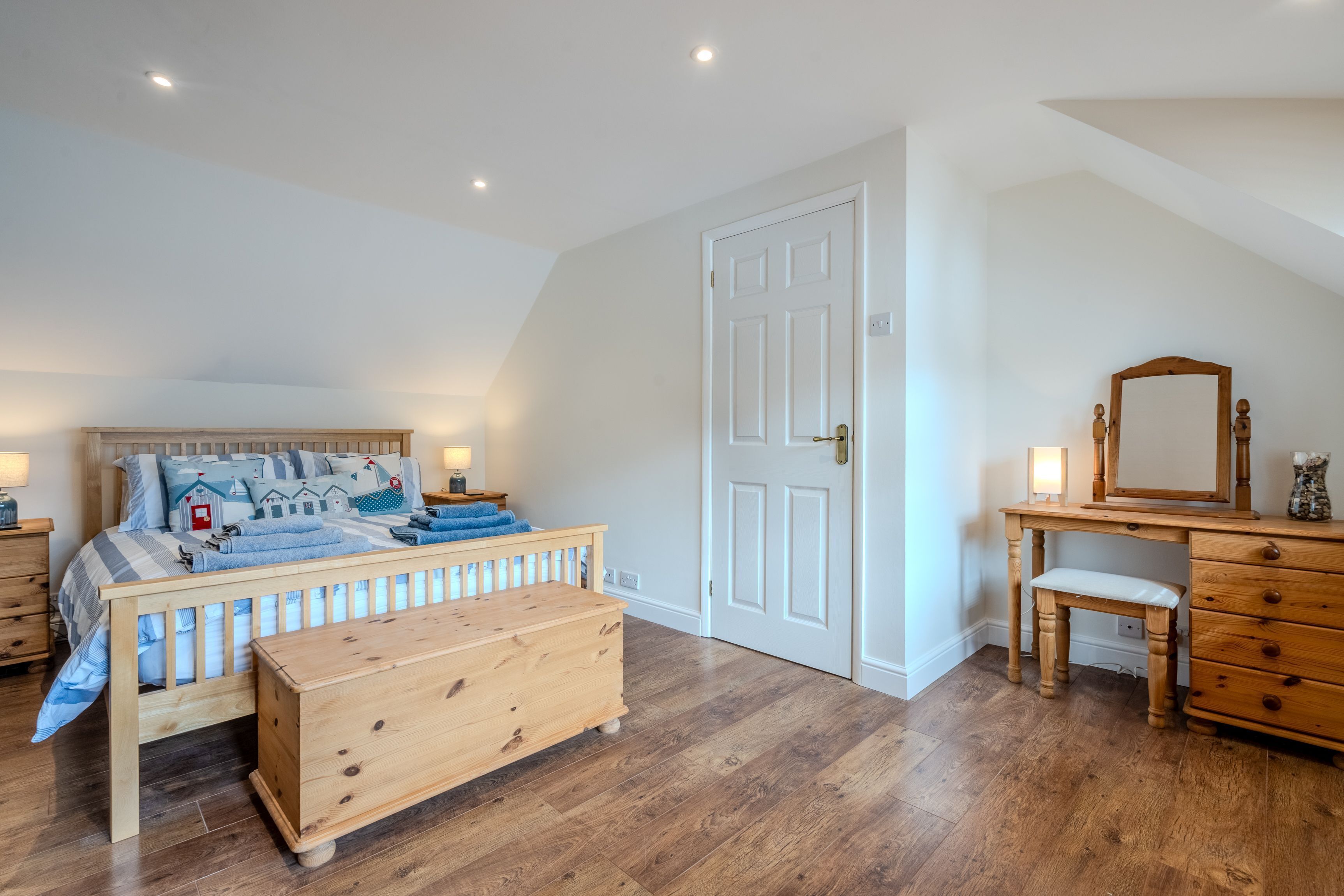 Un dormitorio con cama y banca de madera, cómoda, espejo y puerta.