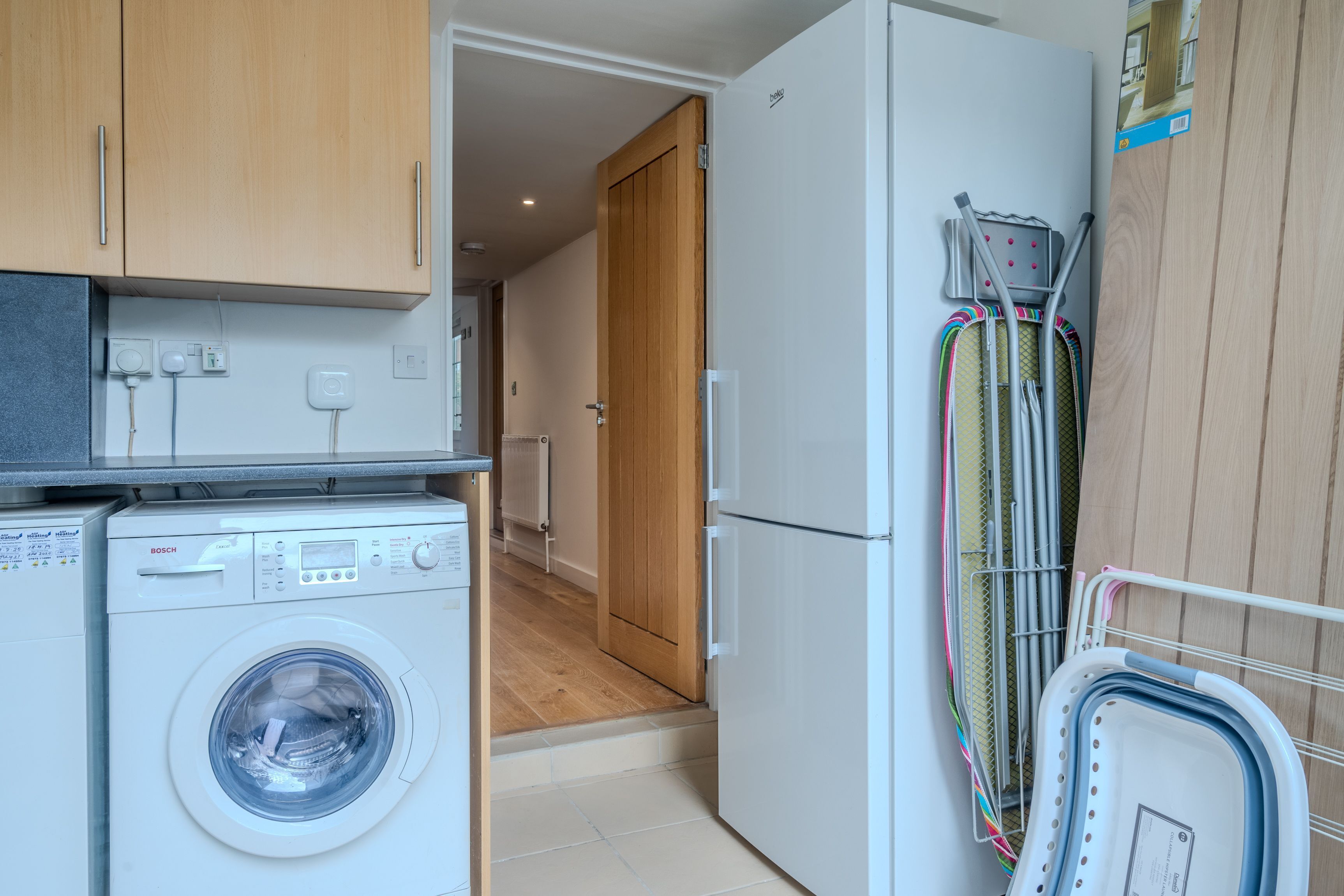 Una cocina compacta con lavadora Bosch, un refrigerador y un tendedero con ropa.