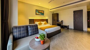 Una habitación de hotel con cama, sofá, una mesita con una planta, ventilador de techo y un cuadro en la pared.