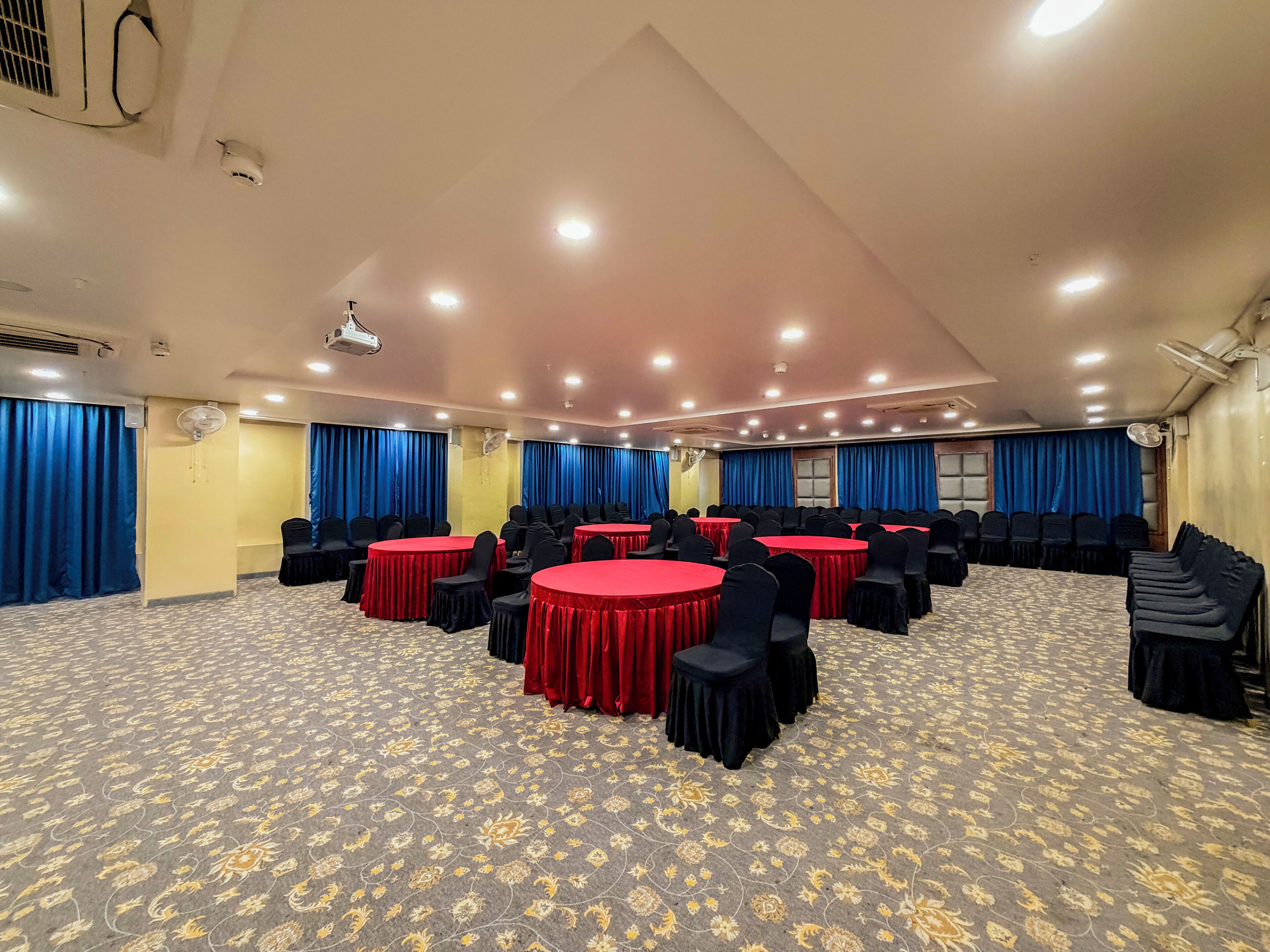 A conference room with round tables, chairs, and blue curtains.