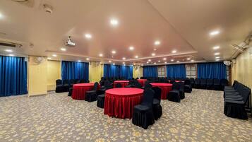 Un salón de conferencias con mesas redondas, sillas y cortinas azules.