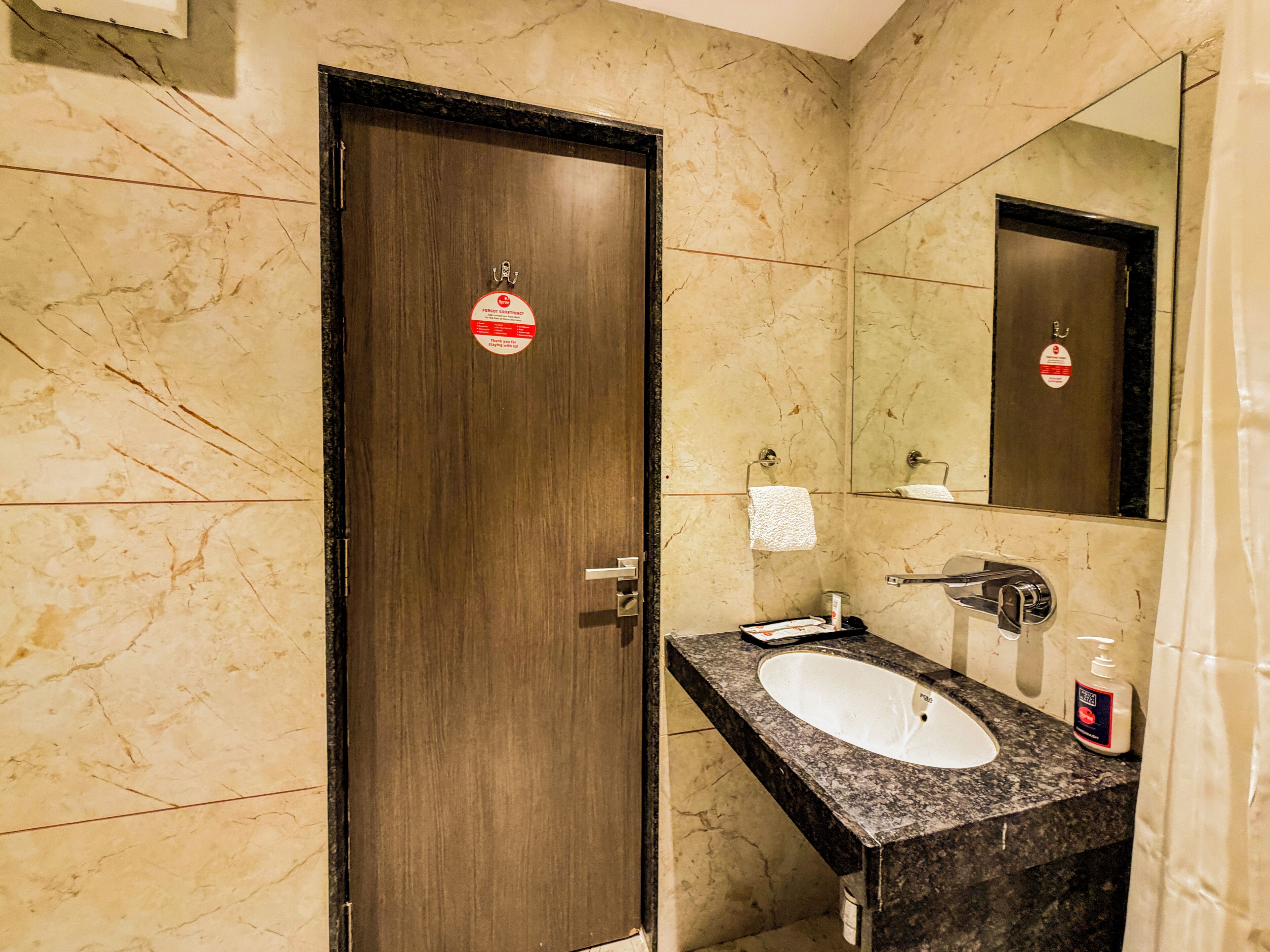 Une salle de bain avec un mur en marbre, une porte en bois, un lavabo avec un miroir et un porte-serviettes.