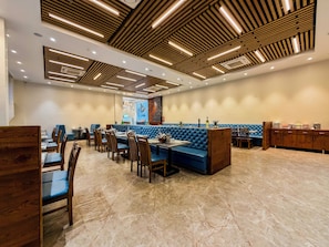 Restaurante com painéis de teto em madeira, cabines acolchoadas em azul e piso de mármore.