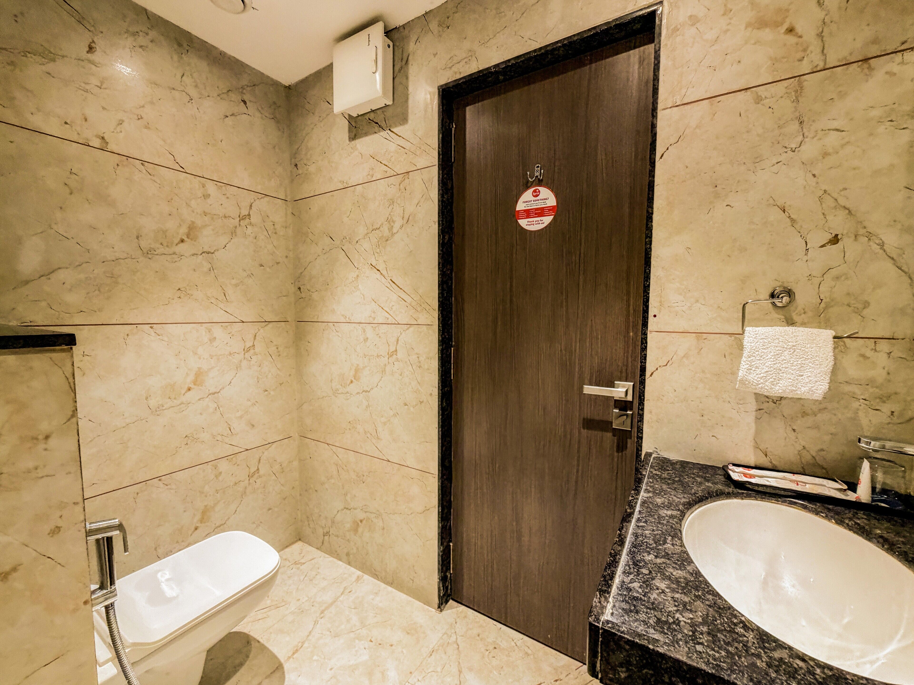 A bathroom with a marble floor, a wooden door, a white sink, and a shower.