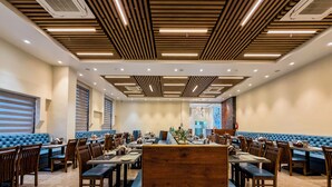 Un amplio comedor con techos de paneles de madera, asientos acolchados azules y suelo de mármol.