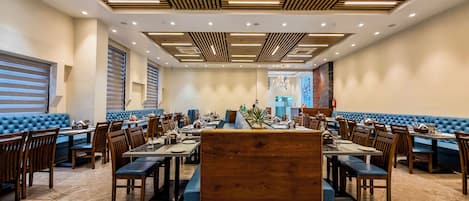 A spacious dining area with wooden panel ceilings, blue cushioned seating, and marble flooring.