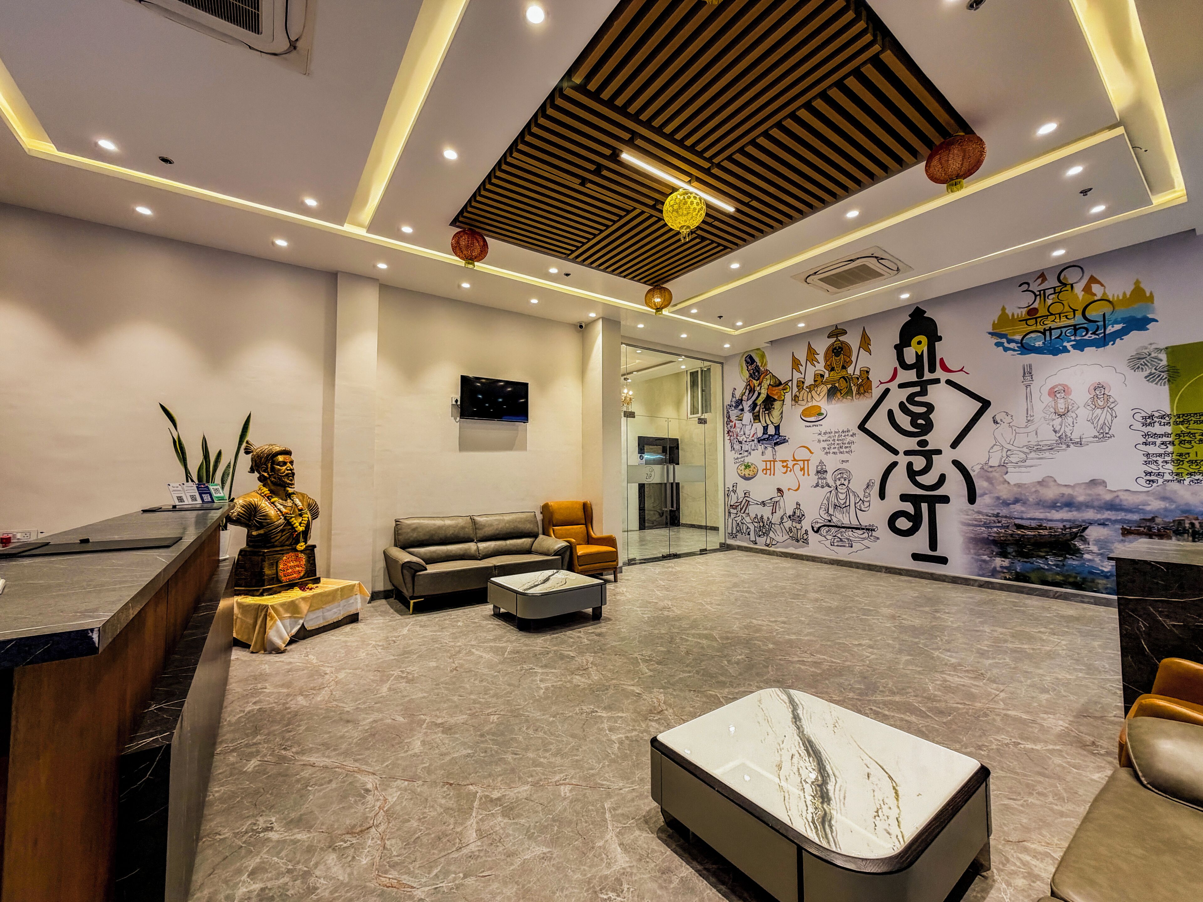 A modern lobby with a reception desk, seating area, and a mural depicting cultural scenes.