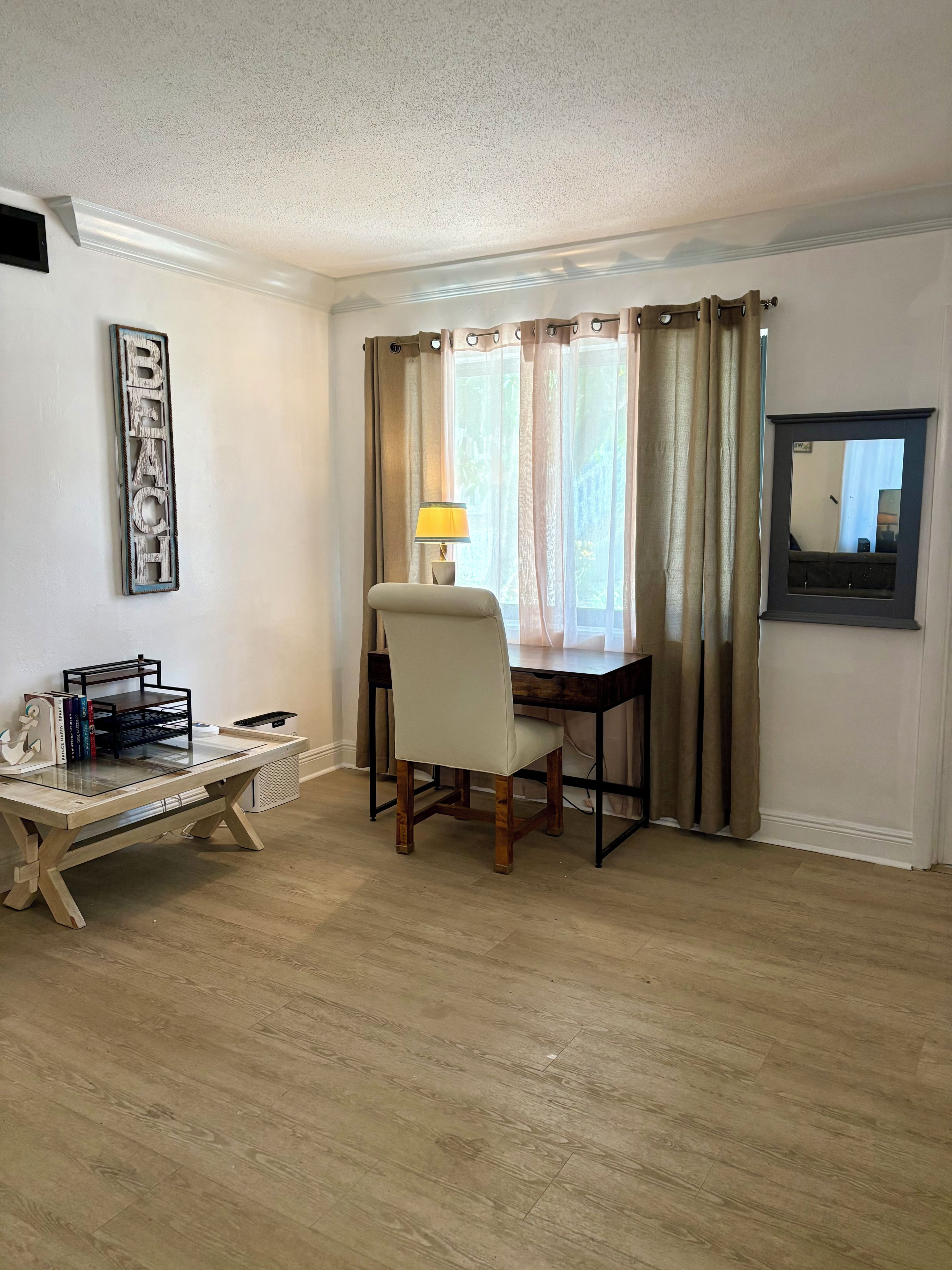 A room with a desk, chair, lamp, and a framed word on the wall.