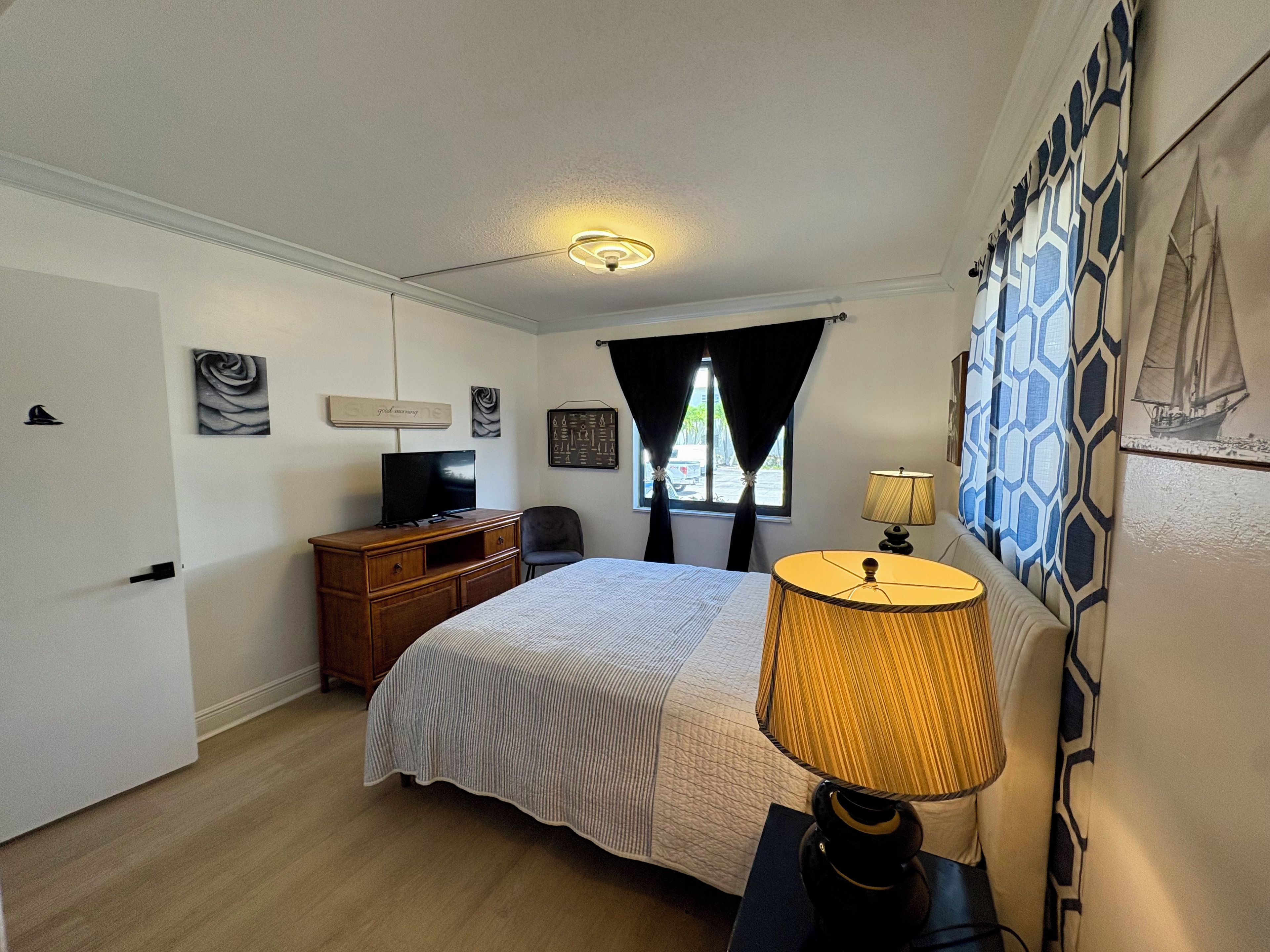 A bedroom with a bed, a desk, a chair, a television, and a lamp.