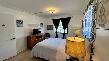A bedroom with a bed, a desk, a chair, a television, and a lamp.