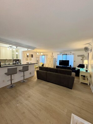 A modern living room with a sofa, a TV, and a dining area with bar stools.
