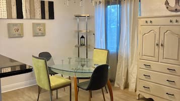 A dining area with a glass table, two chairs, a chandelier, and a white cabinet.