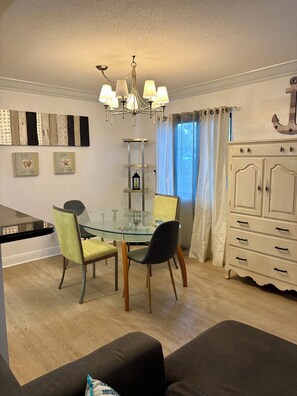 Uma área de refeições com mesa de vidro, duas cadeiras, um lustre e um armário branco.
