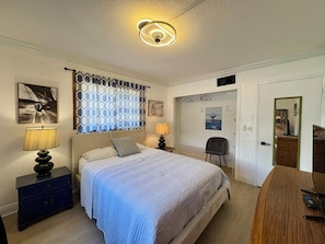 A bedroom with a bed, bedside lamps, a chair, a dresser, and a door leading to another room.
