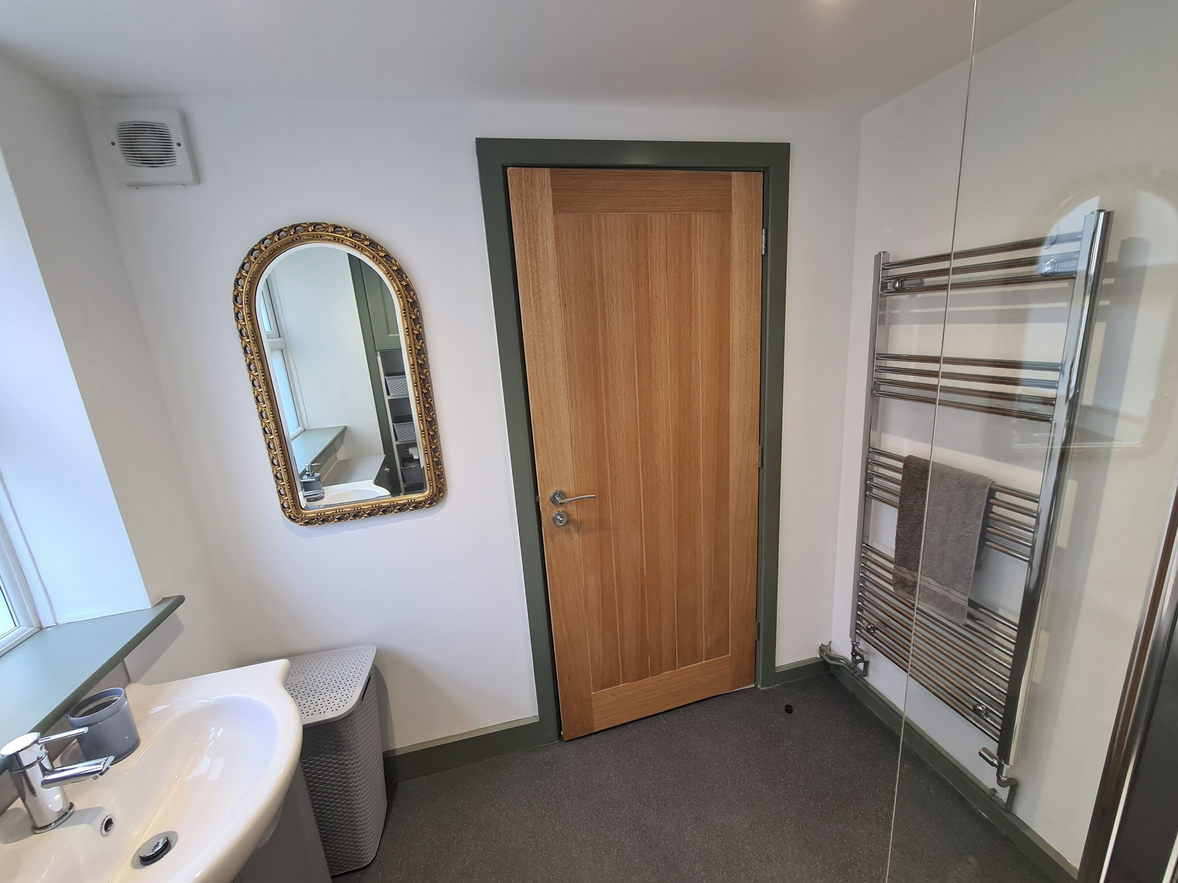Un baño con puerta de madera, un espejo con marco decorativo, un lavamanos con toallero y una cabina de ducha de vidrio.