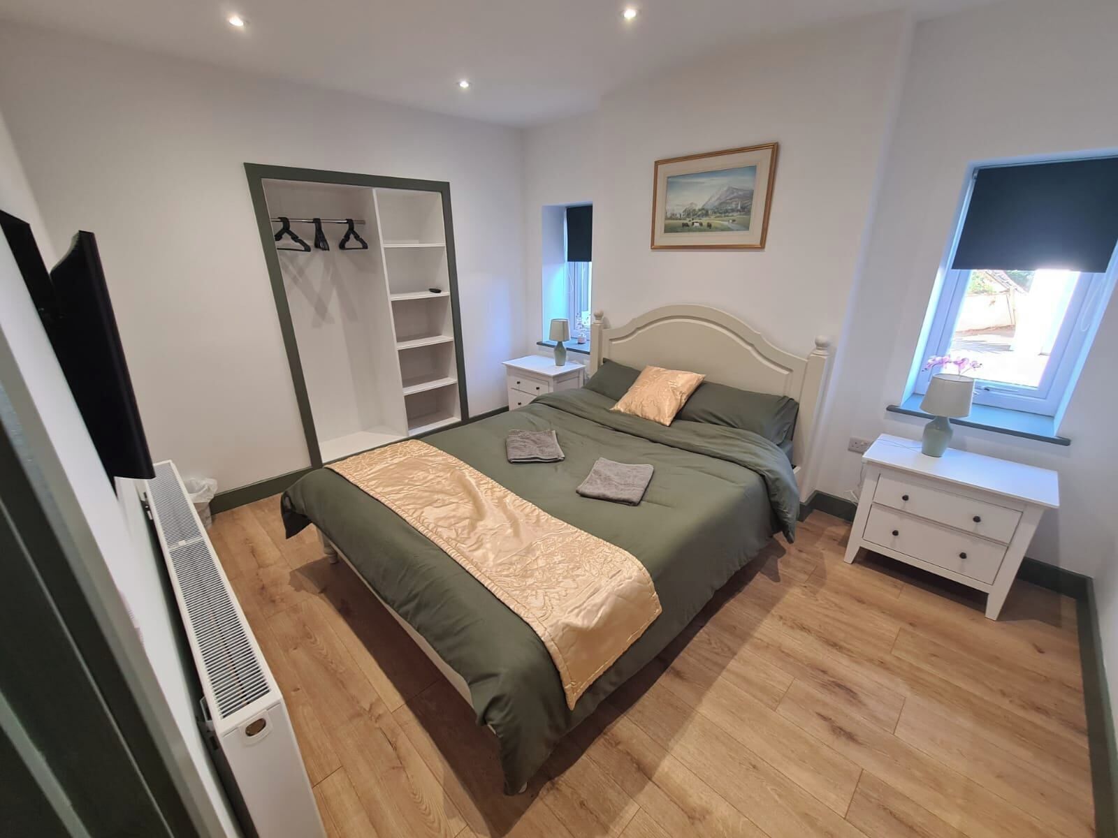 Een slaapkamer met een bed, een kledingkast, een nachtkastje, een raam en een schilderij aan de muur.