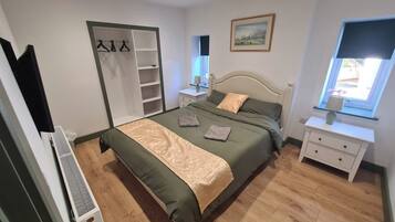 Een slaapkamer met een bed, een kledingkast, een nachtkastje, een raam en een schilderij aan de muur.