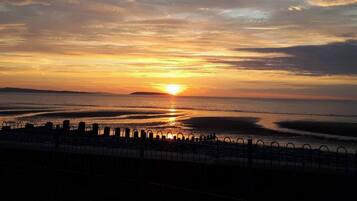Een zonsondergang boven een wateroppervlak, met een metalen hek in de voorgrond.