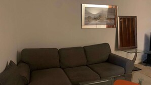 Ein modernes Wohnzimmer mit einem Ecksofa, einem Glastisch und einem gerahmten Kunstwerk an der Wand.