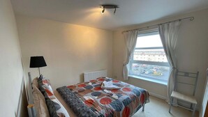 Ein Schlafzimmer mit Bett, Heizkörper, einem Fenster mit Vorhängen, einem Sessel und einer Lampe.