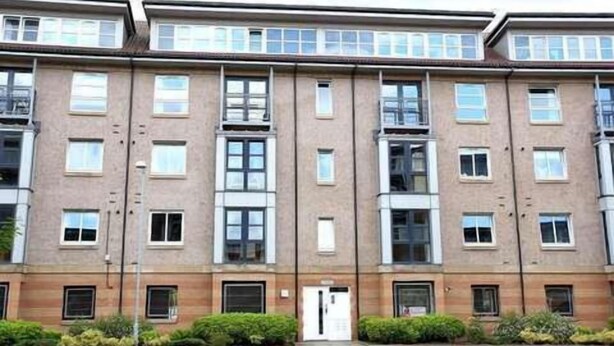 Ein mehrgeschossiges Wohngebäude mit einer symmetrischen Fassade, großen Fenstern und einem zentralen Eingang.