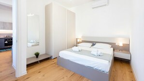 Una habitación de hotel moderna con cama, mesitas de noche, un espejo y una planta pequeña.
