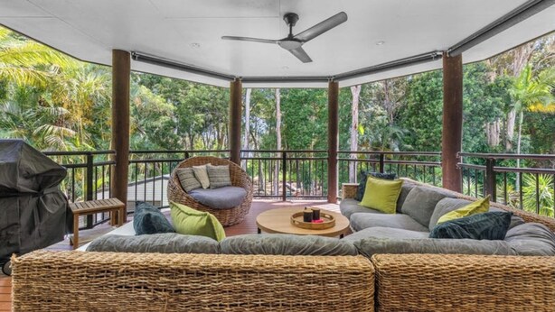 A covered outdoor seating area with wicker furniture, a ceiling fan, and a view of lush greenery. - Toogoom Beach Vibes. Absolute Beachfront Home with pool! 4BR (Toogoom)